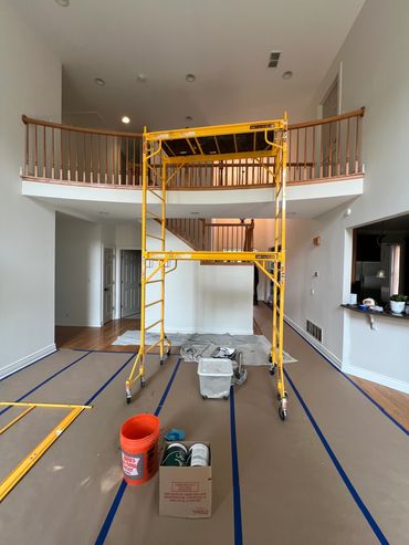 Interior room under renovation with yellow scaffolding and painting supplies.