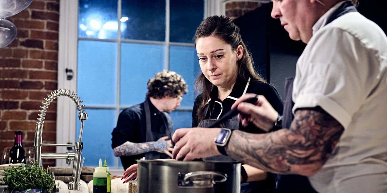 Chefs with tattoos cooking together in a professional kitchen.