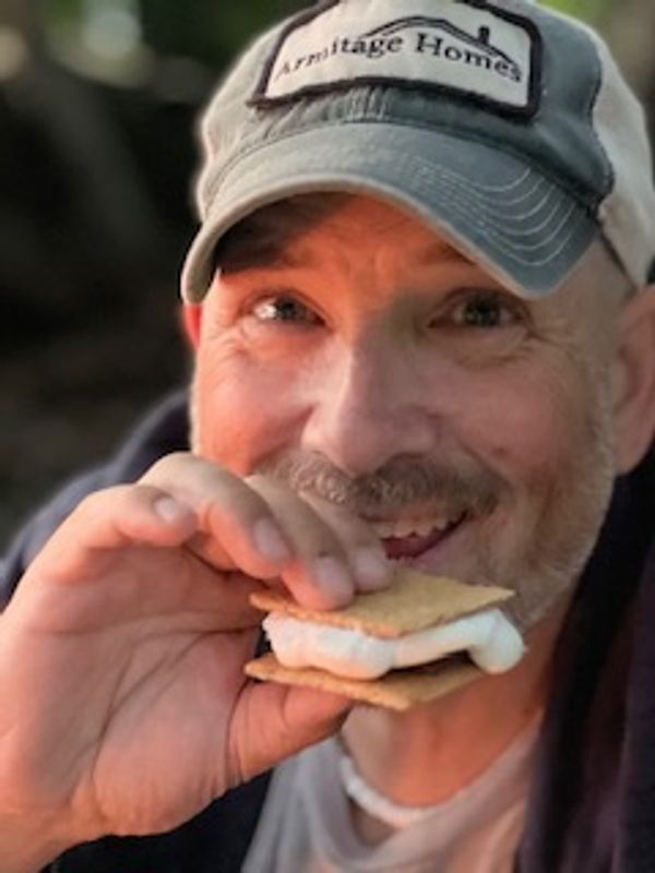 A man smiling while holding a s'more near his mouth.