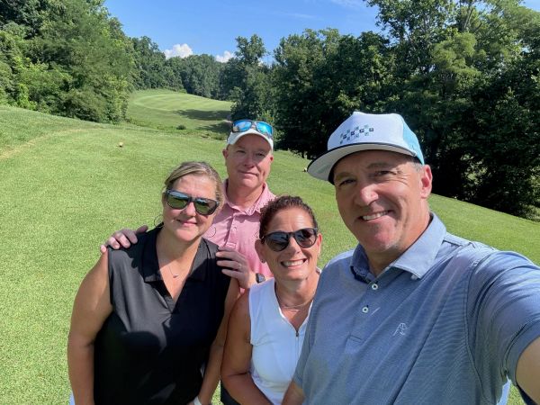 Four friends posing for a selfie on a sunny golf course.