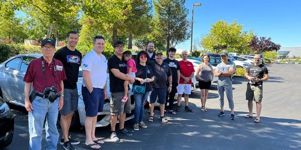 A diverse group of people standing in a parking lot on a sunny day.