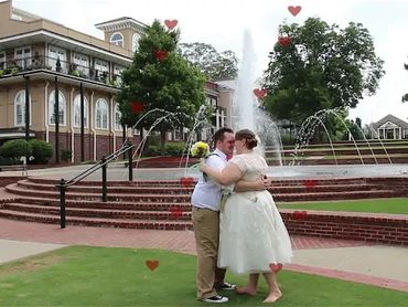 A couple embraces near a fountain with heart decorations in an outdoor park.