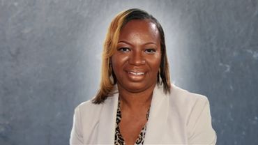 Professional woman smiling in a beige blazer with grey background.