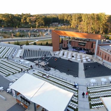 Outdoor amphitheater with stage and seating surrounded by trees.