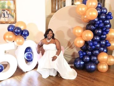 Woman in white dress celebrating 50th birthday with balloons and large number decorations.