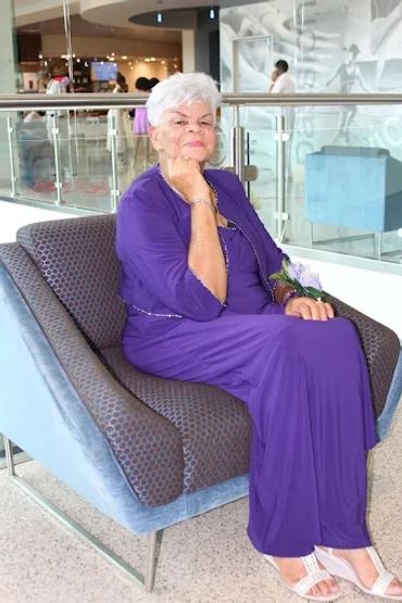 Elderly woman in a purple dress sitting confidently in a modern chair.