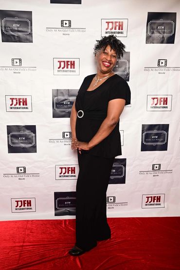 Smiling woman in black dress poses on red carpet at movie event.