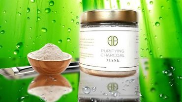 Purifying charcoal mask jar with brush and powder on reflective surface.