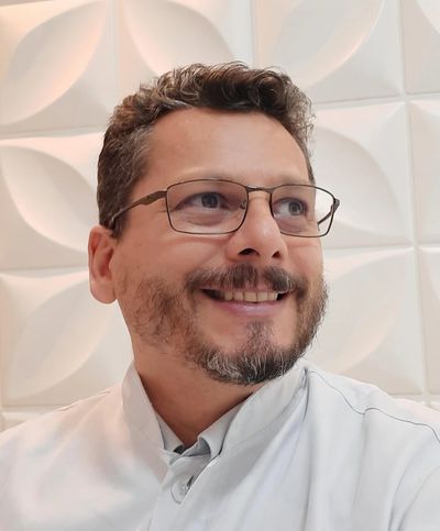 Smiling man with glasses and beard wearing white shirt against a patterned wall.