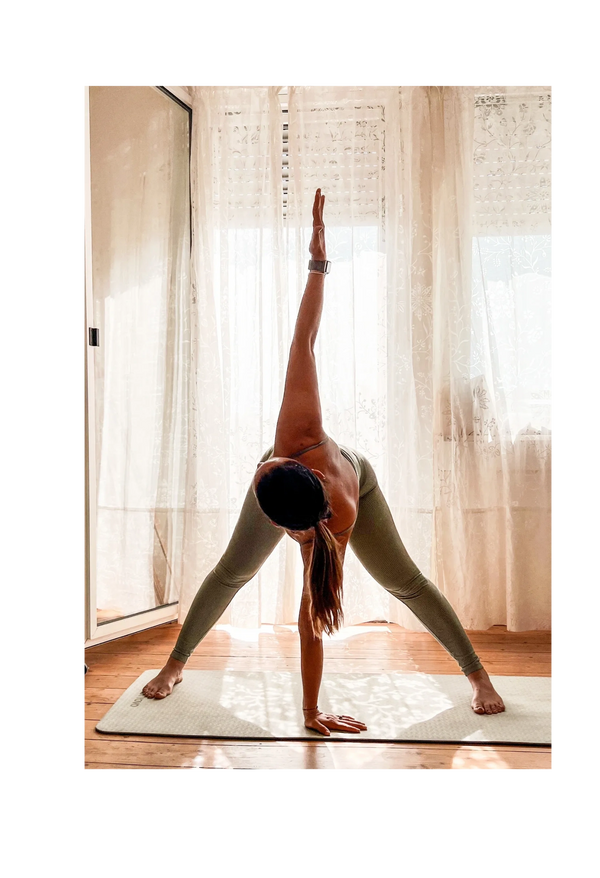 woman doing triangle yoga pose in front of a window and a door with a curtain