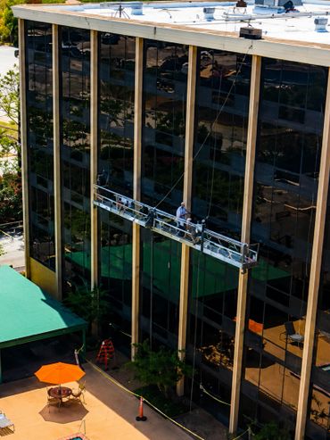Workers cleaning windows on a tall building with a green awning and pool below.