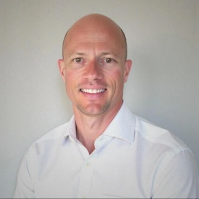 Smiling bald man in a white shirt against a plain background.