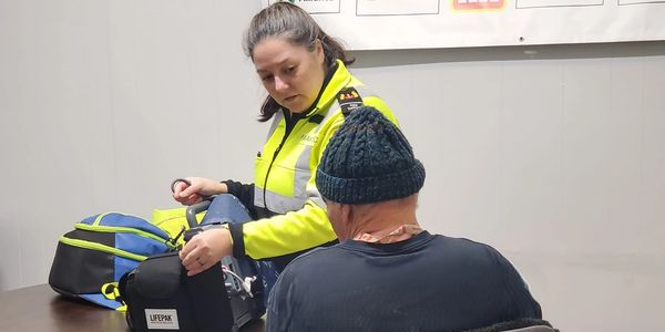 A paramedic assists a seated man wearing a blue knitted hat.