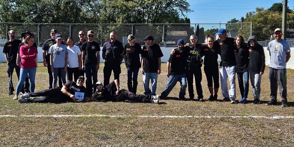 Group photo of people outdoors on a sunny day, some wearing matching black shirts.