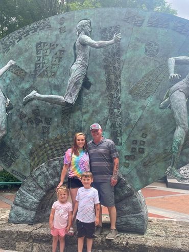 Family posing in front of a large bronze running sculpture outdoors.