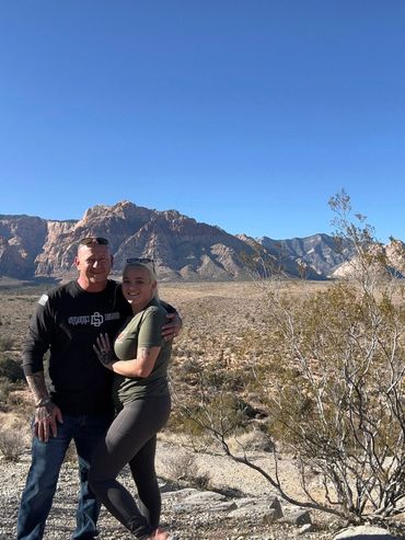 Couple posing happily in a desert landscape with mountains in the background.