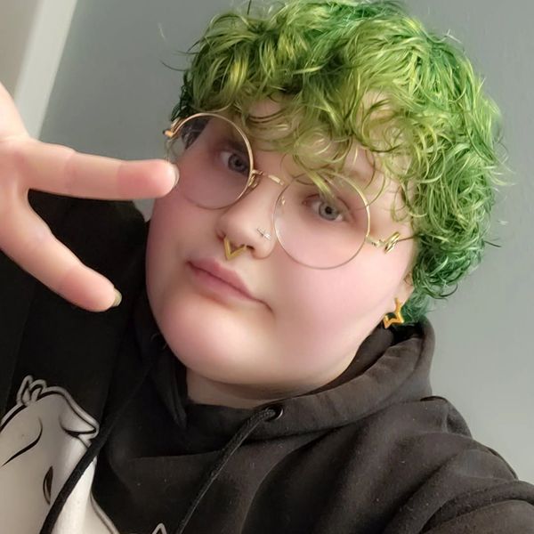 Person with green curly hair making a peace sign.