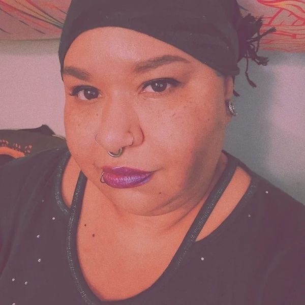 Person with purple lipstick and piercings wearing a black headscarf.