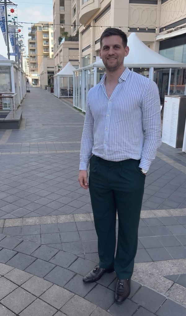 Man in striped shirt and dress pants standing on a tiled walkway.