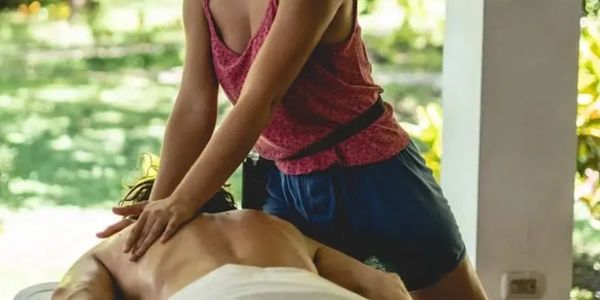 Person giving a back massage outdoors on a sunny day.