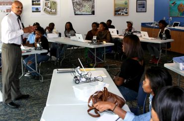 Instructor teaching students in a classroom with laptops and robotics kits.