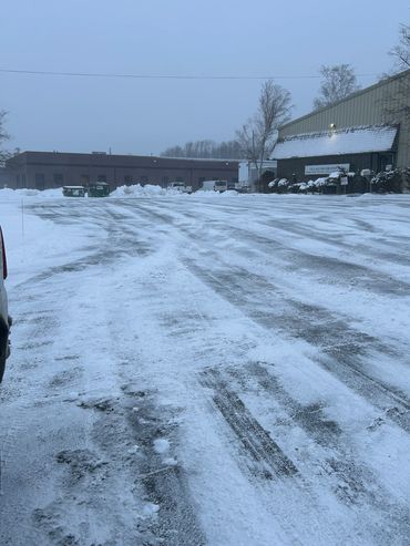 Snow-covered parking lot with tire tracks near buildings.