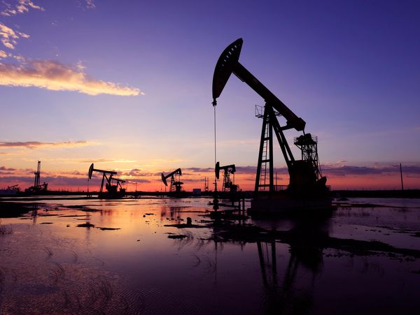 Several oil pumpjacks silhouetted against a vibrant sunset sky over a flooded field.