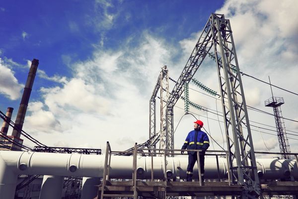 A technician in a hard hat and blue jacket stands on a platform in an industrial setting