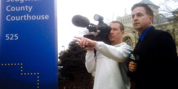 A reporter and cameraman outside a county courthouse preparing for a news segment.