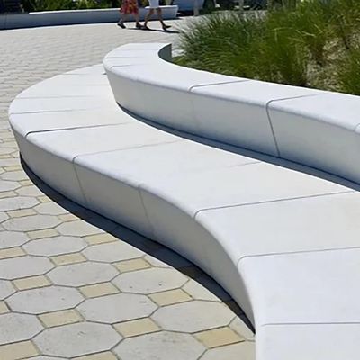 Curved white concrete bench in an outdoor setting with hexagonal pavement.