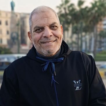 Smiling man in a black jacket outdoors in an urban setting.