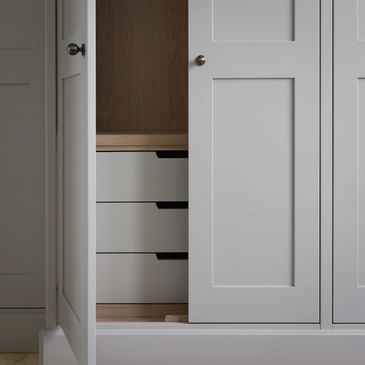 Minimalist white wardrobe with partially open door revealing drawers inside.
