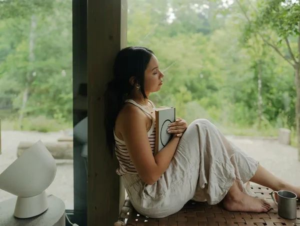 A woman sitting by a window, holding a book.