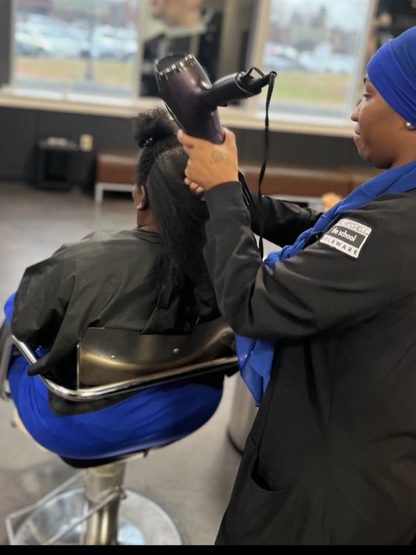 A hairstylist blow-drying a client's hair in a salon.