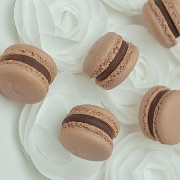 Chocolate macarons arranged on white rose decorations.