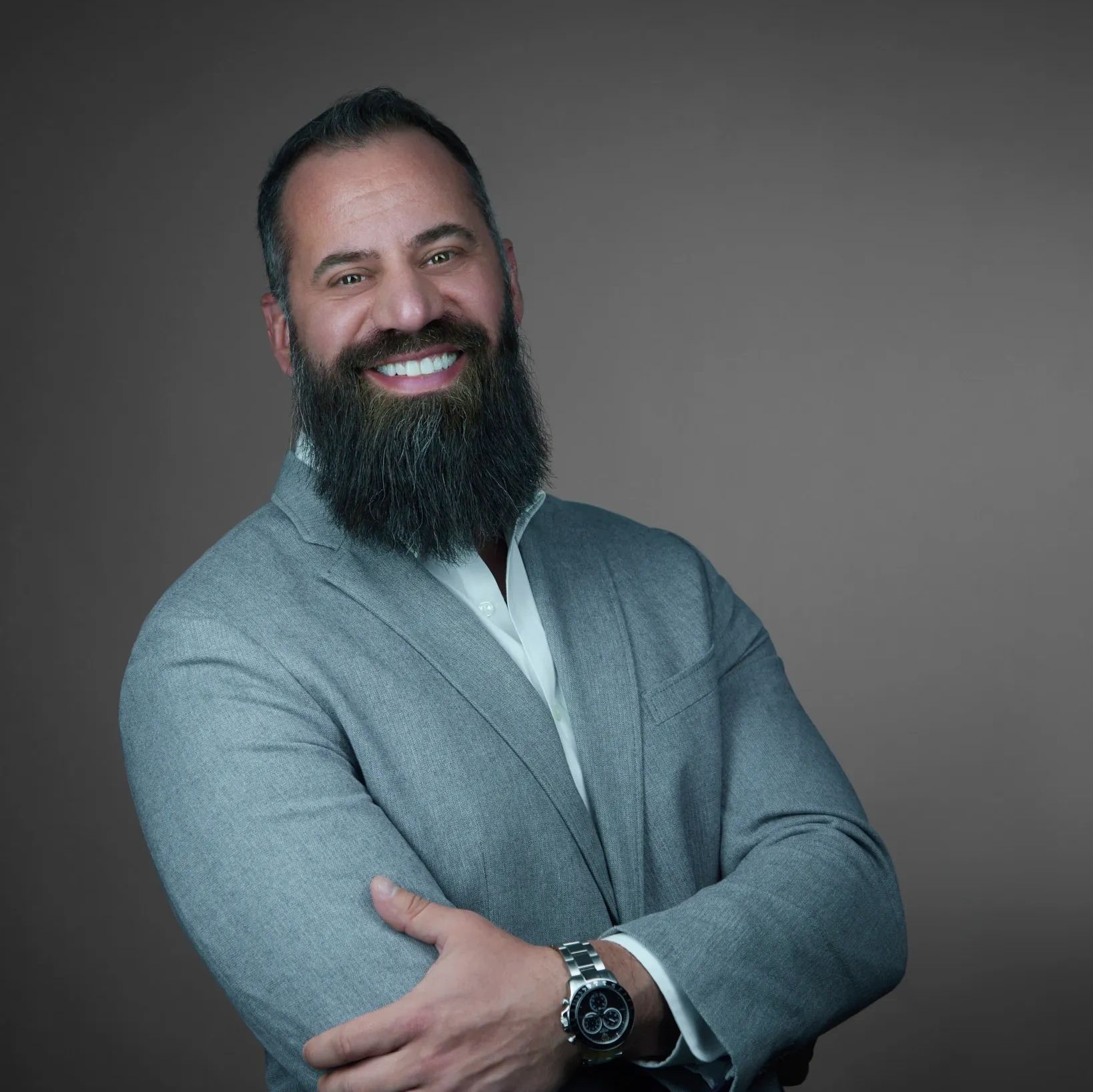 Smiling man with a beard in a gray suit jacket against a plain background.