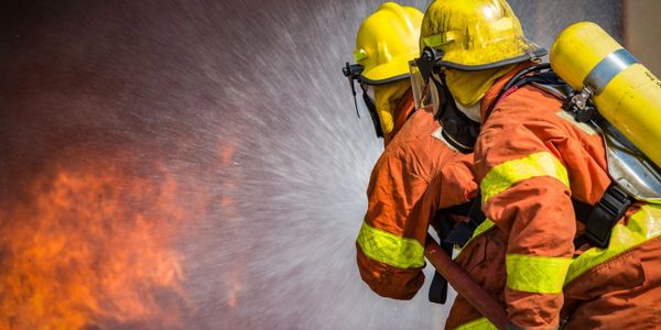 Two firefighters in protective gear extinguish a fire with a hose.