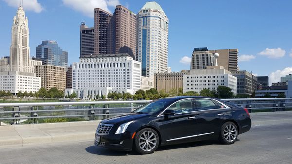 Black luxury sedan parked on a city bridge with skyscrapers in the background.