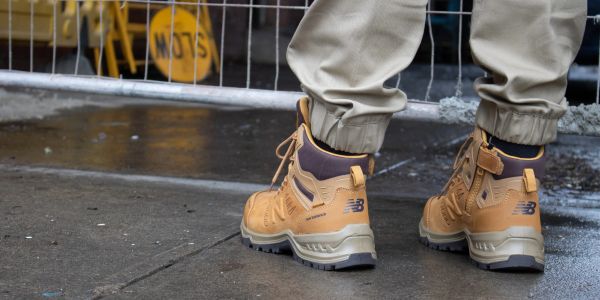 Person wearing tan New Balance boots on wet pavement.