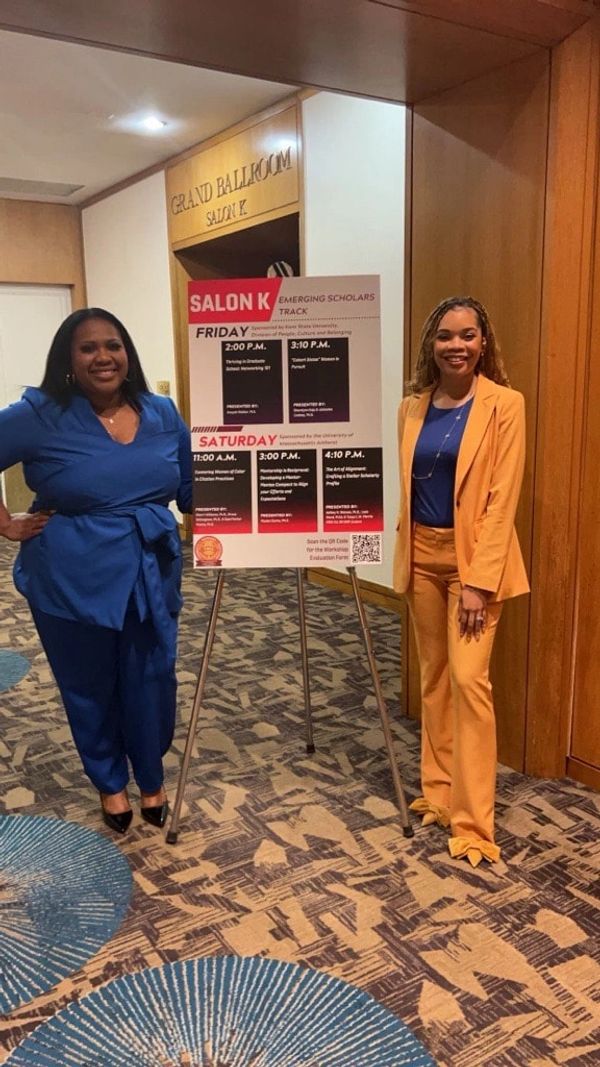 Two women standing by a Salon K event schedule in a conference hallway.