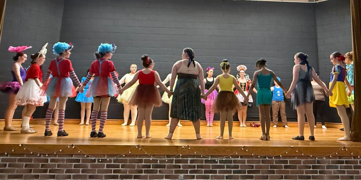 Group of children in colorful costumes holding hands on stage.