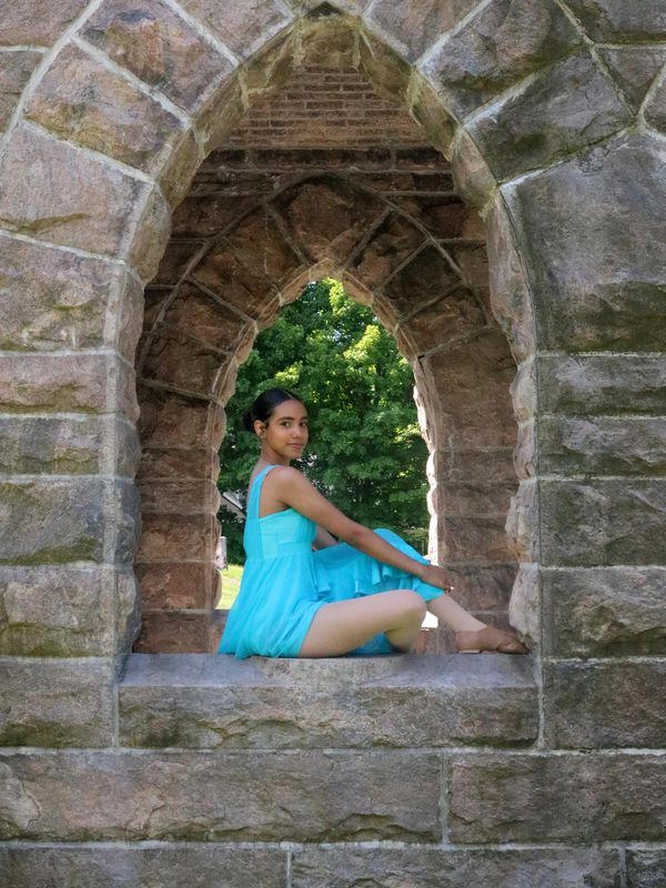A young woman in a blue dress poses in a stone archway.