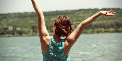 Joyful woman by the sea, with her arms raised in celebration
