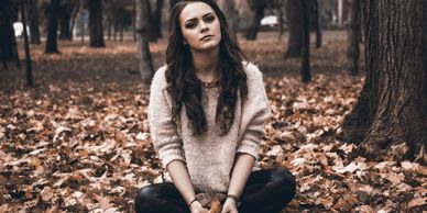 Anxious woman sitting cross-legged in amongst fallen autumn leaves