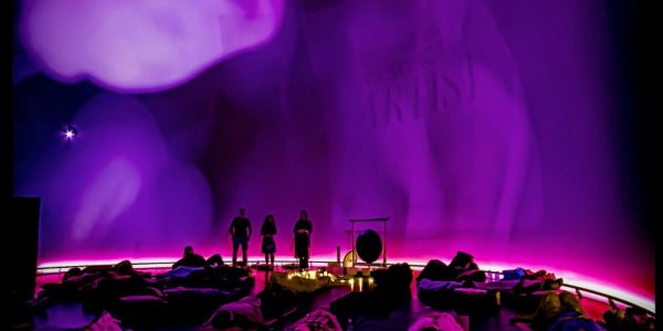 People in a dark room with purple lighting and a large screen.