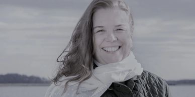 Smiling woman outdoors with a scarf and quilted jacket.