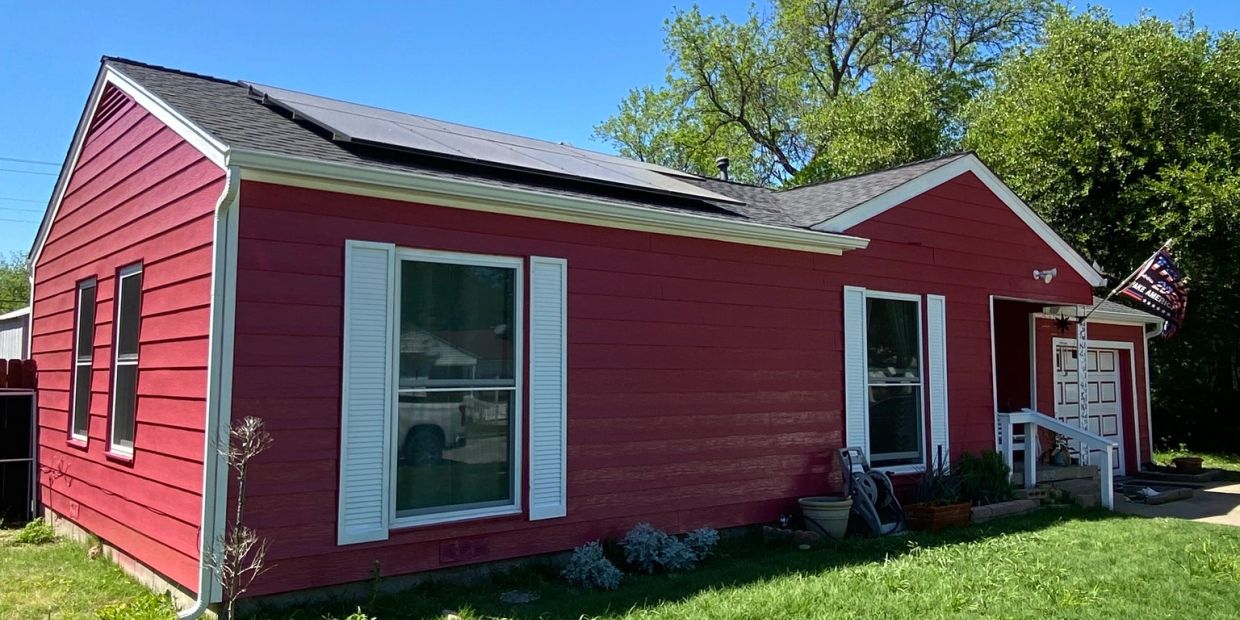 Red house with solar panels on the roof and white window shutters.