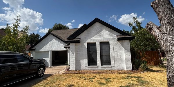 White brick house with a black roof and closed windows.