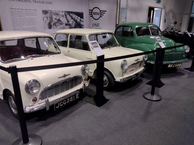 Three vintage Mini cars displayed behind a barrier in a museum.