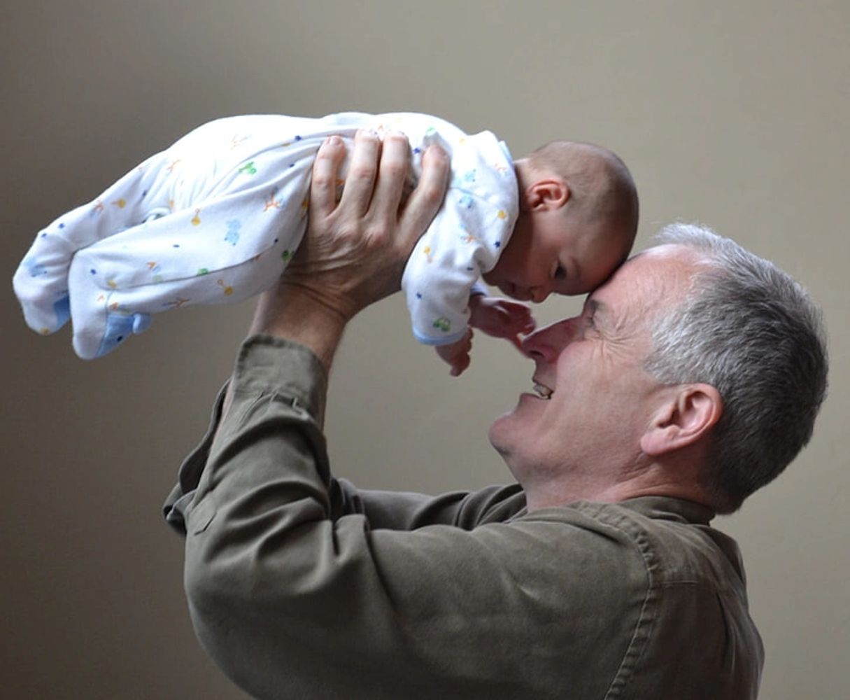 Older man joyfully holding baby close to his face.